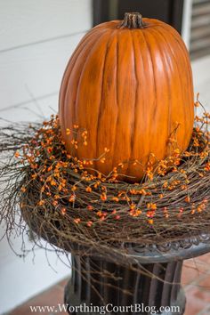 an orange pumpkin sitting on top of a metal pole next to some twigs and berries