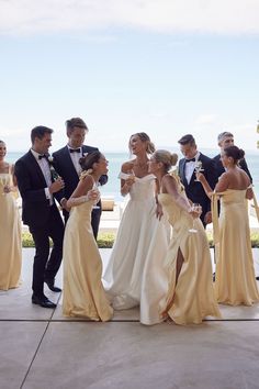 a group of people standing next to each other on a sidewalk near the ocean with champagne in their hands