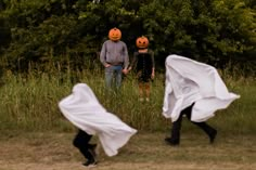 two people in halloween costumes are walking through the grass with white cloths on their heads