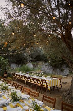 an outdoor dining area with tables and chairs set up for dinner under the shade of a tree