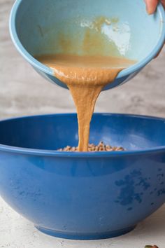 a person pouring peanut butter into a blue bowl