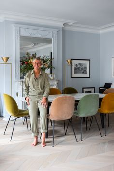 an older woman sitting at a table in a room with chairs and paintings on the walls