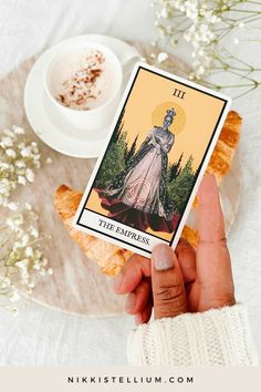 a person holding up a tarot card next to a cup of coffee and pastry