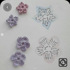 four crocheted flowers sitting on top of a white table next to each other