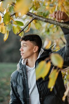 a young man standing under a tree in the fall