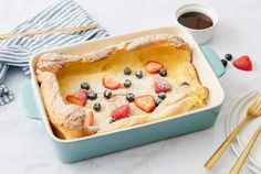 a blue casserole dish with berries and powdered sugar on top, next to a cup of coffee