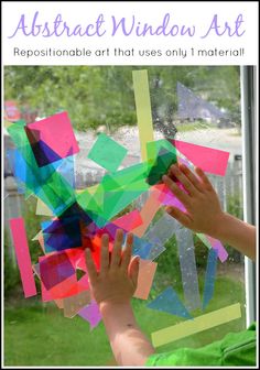 a child's hand reaching out to paint on a window with colorful paper squares