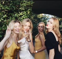 four beautiful young women standing next to each other holding wine glasses in their hands and laughing