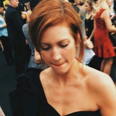 a woman in a black dress is looking at her cell phone while people walk by