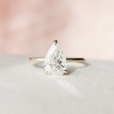 a pear shaped diamond ring sitting on top of a white cloth covered surface with a pink background