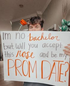 a man holding up a sign that says i'm no bachelor but will you accept this rose and be my prom date?