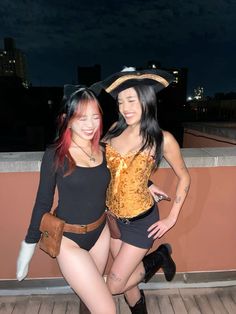 two women dressed up in costumes posing for the camera on a roof top deck at night