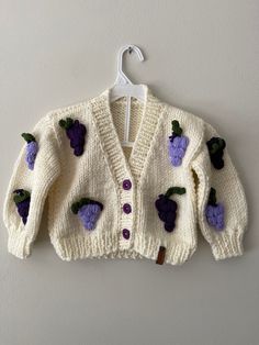 a white sweater with purple flowers on it hanging from a hanger against a wall