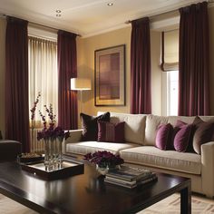 a living room filled with furniture and windows covered in maroon draping next to a coffee table