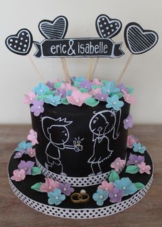 a black cake with pink, blue and green flowers on top that says eric & isabielle