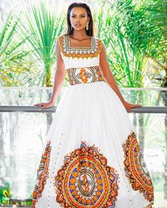 a woman in a white and orange dress standing on a balcony with palm trees behind her