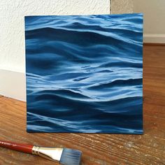 an acrylic painting of blue water on a wooden floor with a brush next to it