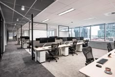 an empty office with desks and chairs in the foreground, windows to the other side