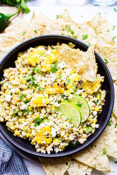 a bowl filled with corn and cilantro next to tortilla chips