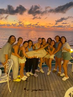 a group of women standing on top of a wooden deck next to the ocean at sunset