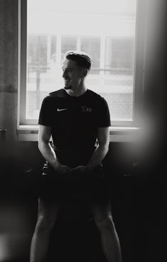 a black and white photo of a man sitting in front of a window