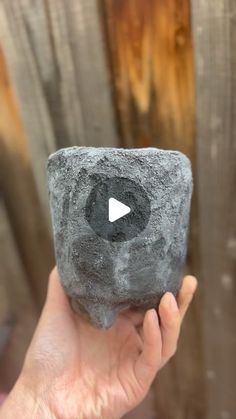 a person holding up a rock with a video playing button on it's side