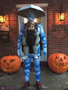 a man with an umbrella and goggles standing in front of two pumpkins