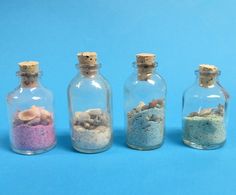 five miniature bottles filled with sand and sea shells on a blue background, each containing an individual's own message