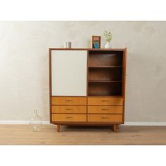 a wooden cabinet with two doors and three drawers on the bottom, in front of a white wall