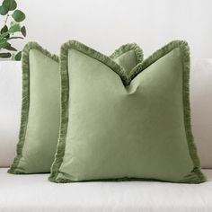 two green pillows sitting on top of a white couch next to a potted plant