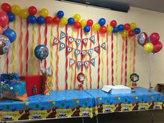 a birthday party with balloons and streamers on the wall behind a blue table cloth