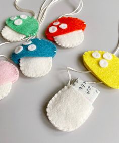 four felt ornament shaped like mushrooms with tags attached to the strings on a table