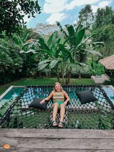 a woman sitting on top of a wooden deck next to a pool in the jungle