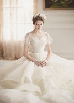 a woman in a white wedding dress sitting on a bed with her hands clasped to her knees