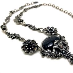 "Black cabochon stone with leaves and skulls with Black crystal eyes Flowers with Black crystal centers & Vitrail crystal details around Adjustable length 14-18\" Lead free pewter Always ethically sourced bones. Nothing has ever been harmed for the purpose of our jewelry. All pieces are made-to-order despite the \"in stock\" number in the listing. Time frame varies from piece to piece so please message us if you need something by a certain date and we will do our best. A portion of our profi Gothic Silver Oval Necklace, Victorian Necklace, Crystal Eyes, Cabochon Necklace, Crystal Eye, Black Crystals, Oval Cabochon, Art Fair, Amazing Jewelry