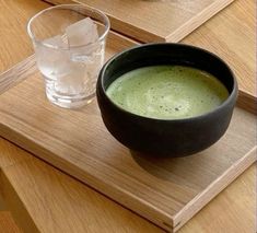 a bowl of broccoli soup next to a glass of water on a wooden tray