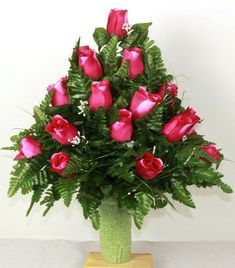 a green vase filled with pink roses on top of a table