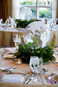 the table is set with silverware and greenery for an earth globe centerpiece