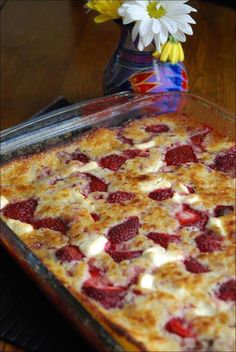 a dessert dish with strawberries and cream in it sitting on a table next to a flower vase