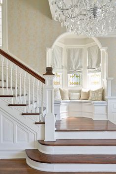 a white staircase with chandelier and pillows on the top step in front of it