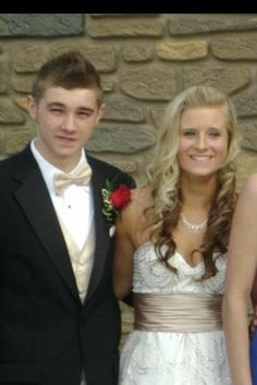 three people standing next to each other in front of a stone wall wearing formal attire