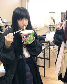 a woman with long black hair eating yogurt and chopsticks