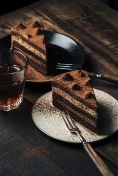 two slices of chocolate cake sitting on plates next to a glass of tea and fork