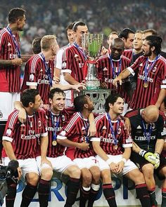 a group of men sitting on top of a soccer field with a trophy in front of them