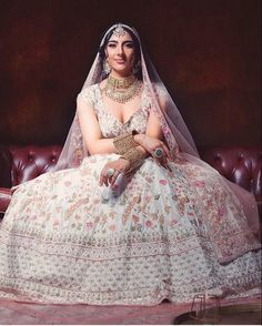 a woman in a wedding dress sitting on a couch with her hands clasped to her chest