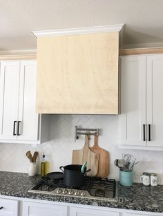 a stove top oven sitting under a wooden cabinet above it's cooking utensils