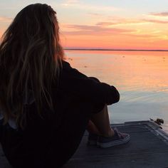 a woman sitting on the edge of a dock looking out at water with an inspirational quote above her