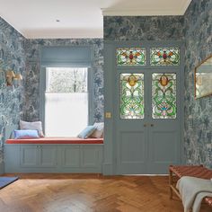 a room with blue wallpaper and wooden flooring, two stained glass windows on either side of the door