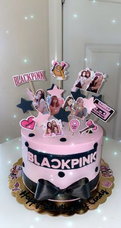 a pink and black birthday cake with pictures on the top is sitting on a table