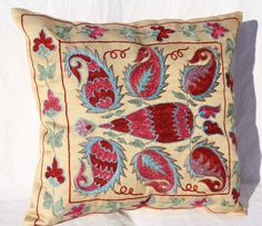 an embroidered pillow with red and blue designs on it's sides, sitting on a white background